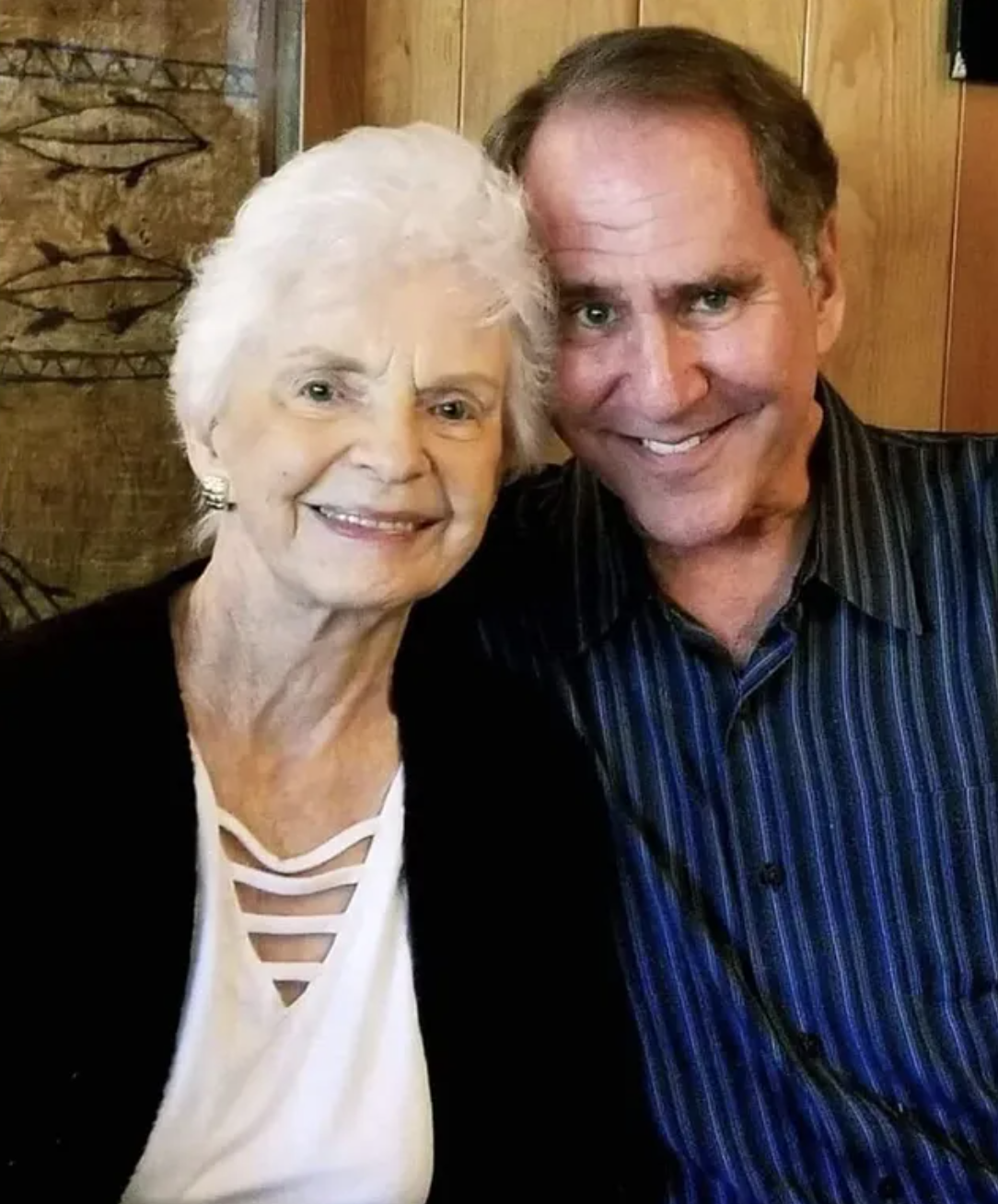 Robert Rand smiling cheek to cheek with Joan VanderMolen, Kitty Menendez’s sister, her white hair bright against warm wood paneling.